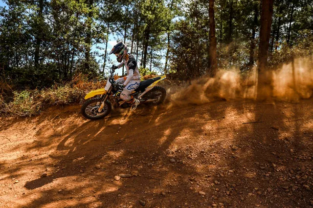 A rider throws a wall of red dust off a berm on a forest motocross track.
